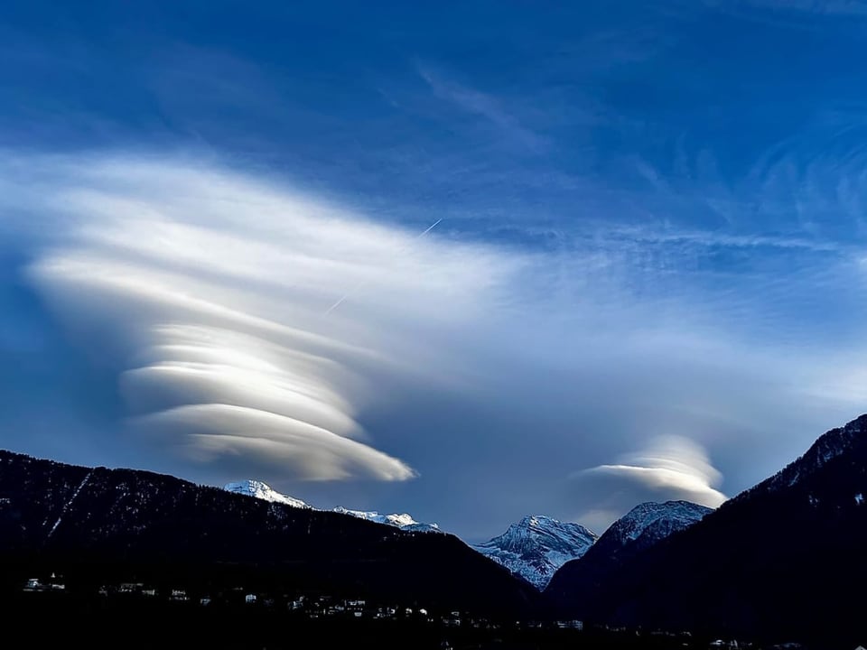 Linsenförmige Wolken über schneebedeckten Bergen bei blauem Himmel.