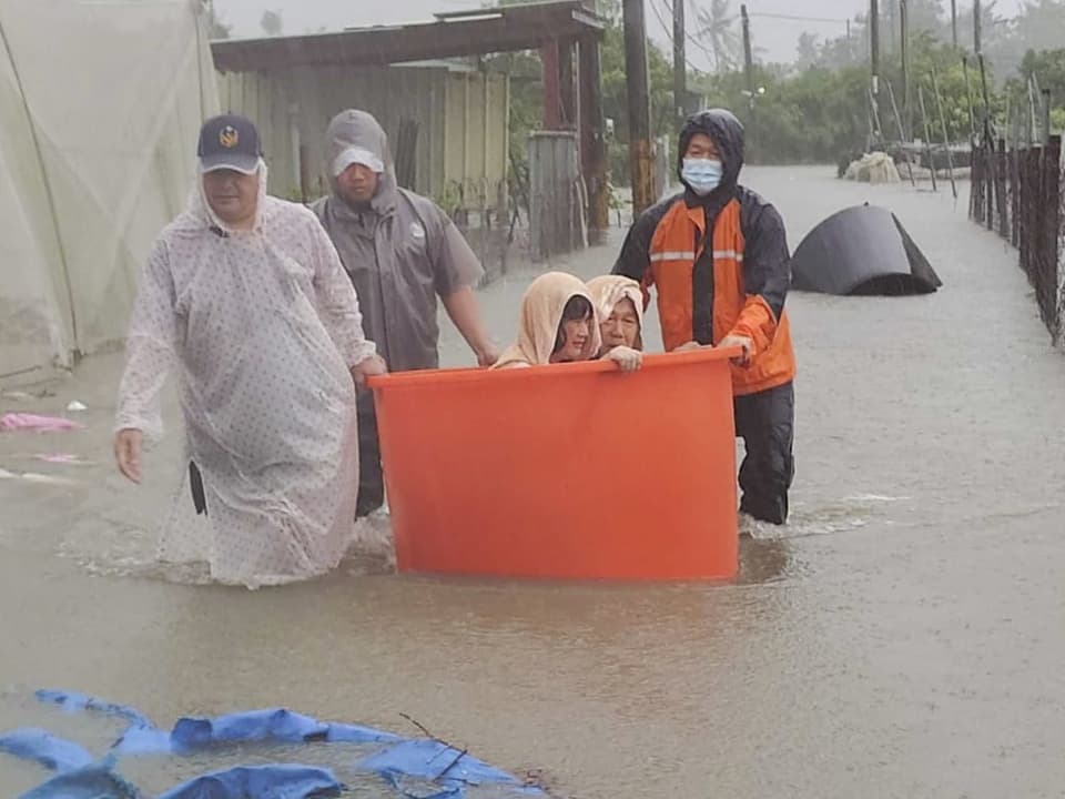 Rettungskräfte evakuieren Kinder bei Überschwemmung in orangener Wanne.