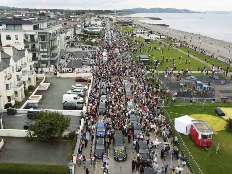 Blick von oben auf Hunderte Menschen auf einer Strasse, die einem Strand entlang führt