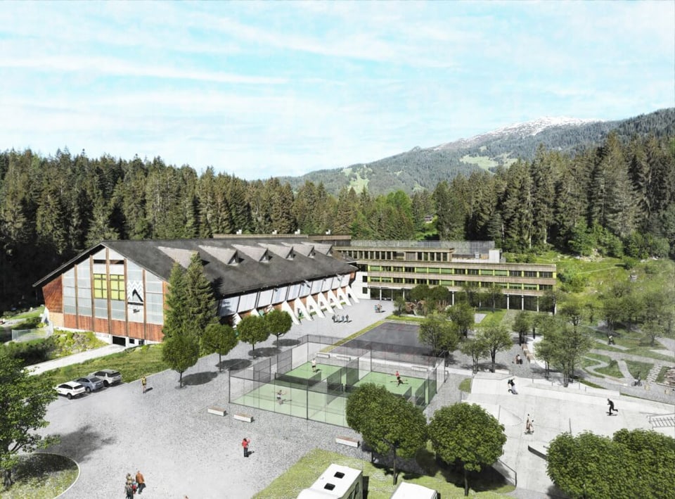 Luftaufnahme eines Gebäudekomplexes im Grünen, umgeben von Bäumen und Bergen.