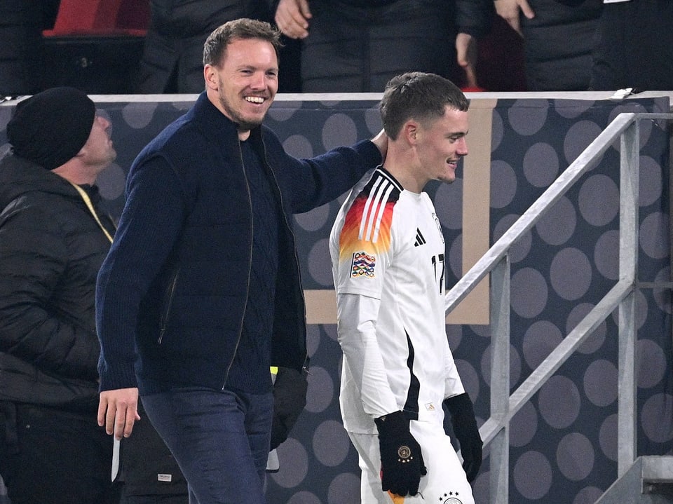 Mann lächelt und legt Arm um Fussballspieler im Stadion.