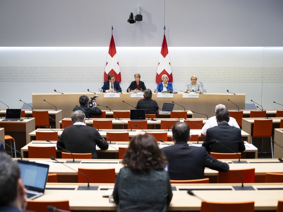 Pressekonferenz in einem modernen Konferenzraum mit zwei Schweizer Flaggen.