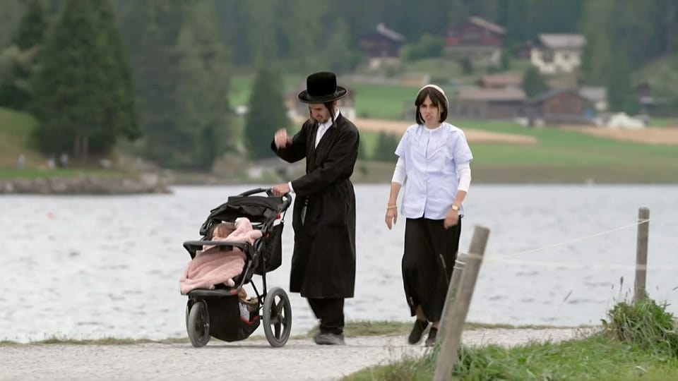 Jüdisch-orthodoxes Paar spaziert mit Kinderwagen am See.