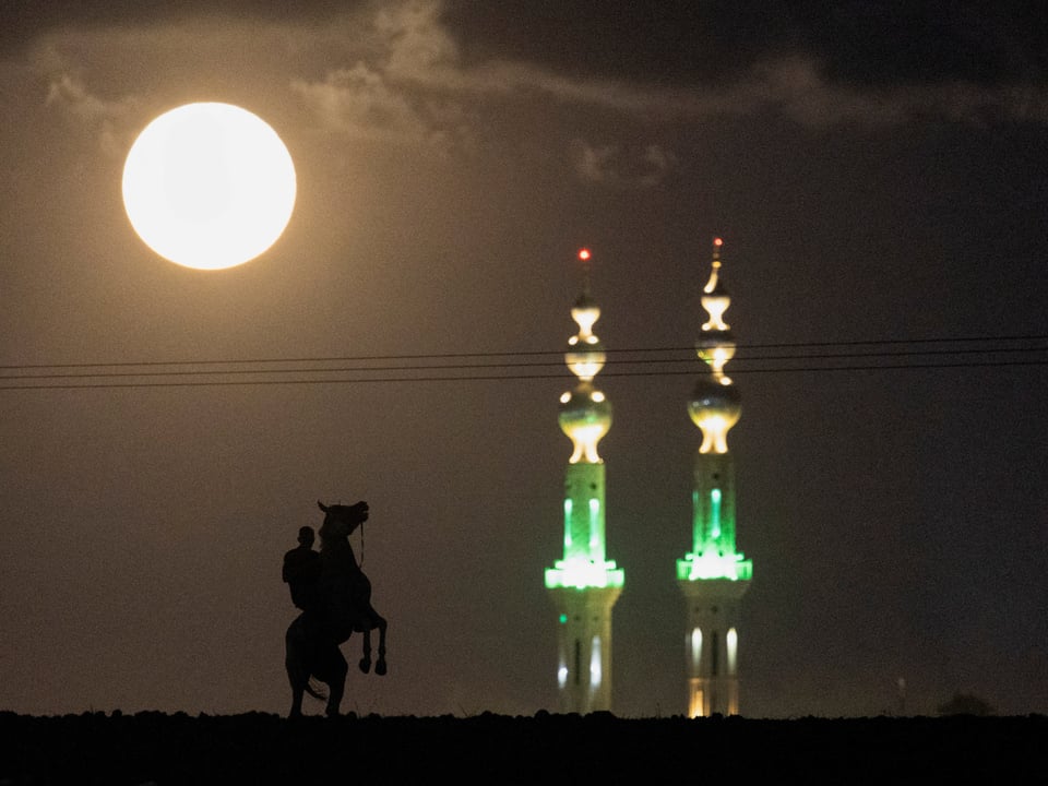 Reiter vor zwei beleuchteten Minaretten und Vollmond.