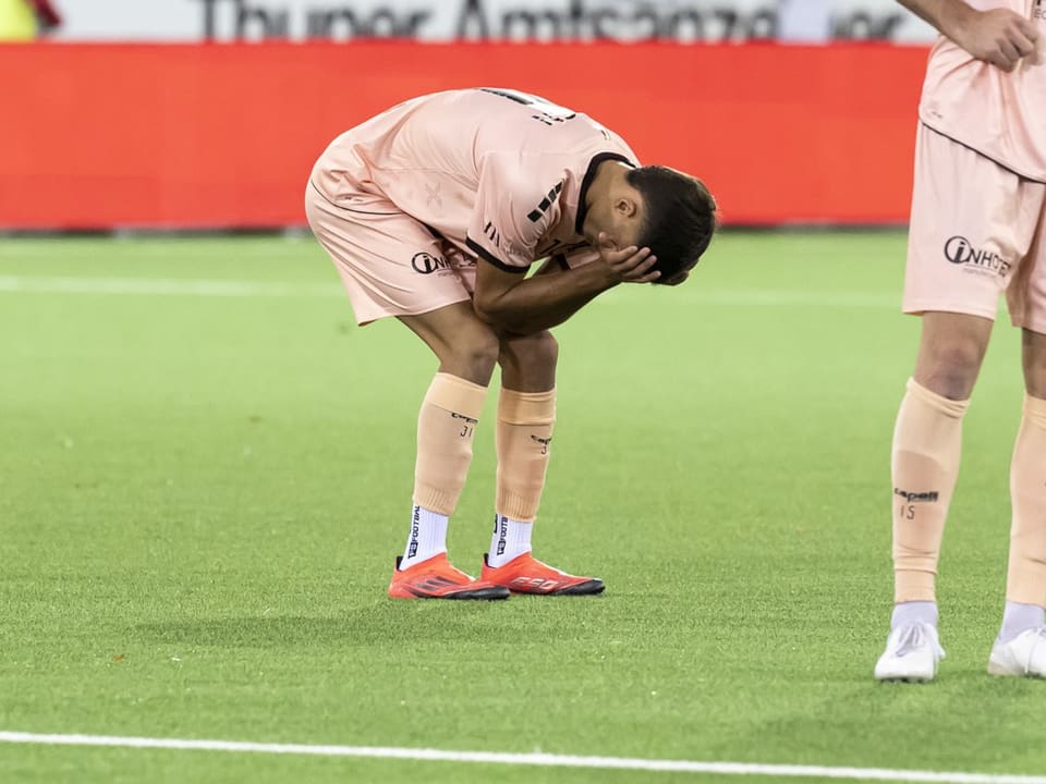 Fussballspieler beugt sich enttäuscht nach vorne, hält Kopf in Händen.