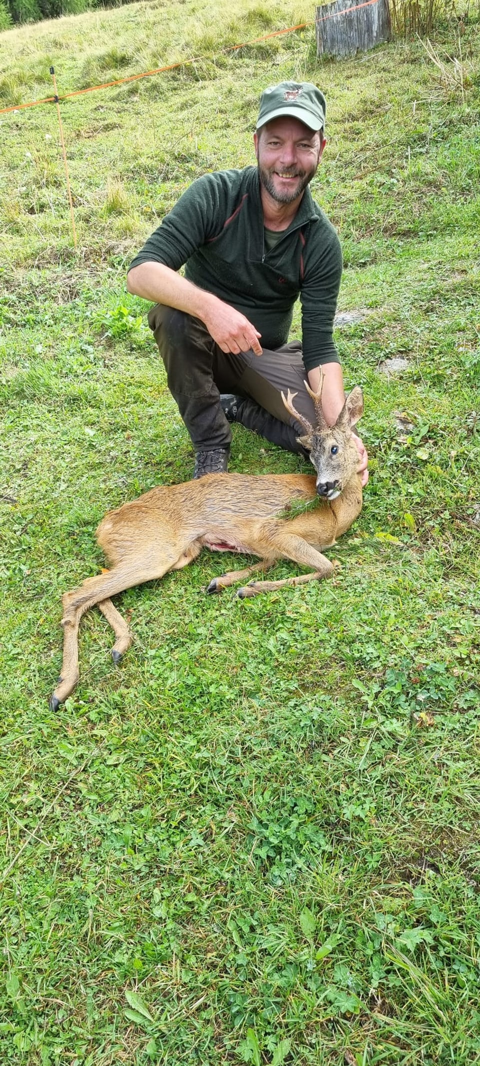 Mann posiert mit erlegtem Reh auf einer Wiese.