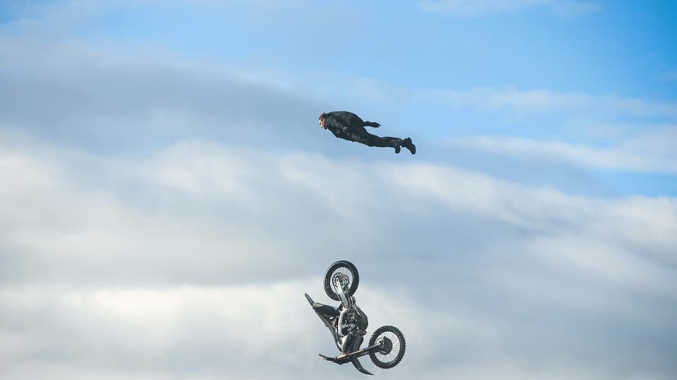 Ein Mann fliegt durch die Luft, unter ihm fällt ein Motorrad Richtung Erde.