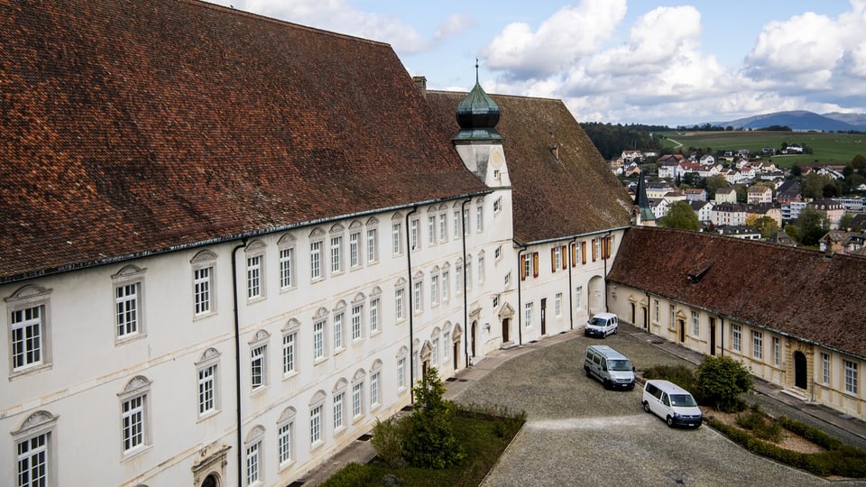 Schloss Pruntrut: Historisches Gebäude mit roten Ziegeldächern und Autos im Hof.