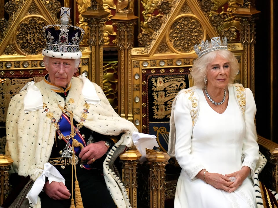 Zwei gekrönte Personen in prächtiger Kleidung auf königlichen Thronen.