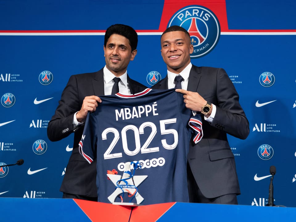 Zwei Männer halten ein PSG-Trikot mit 'Mbappé 2025'.