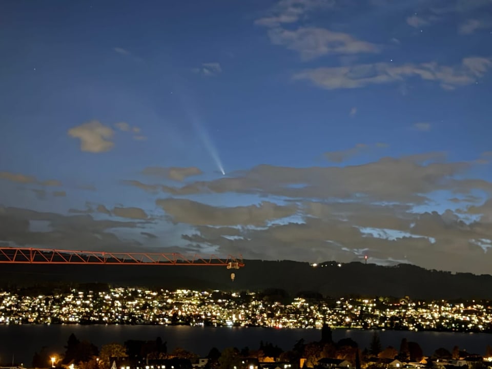 Himmel mit Komet über beleuchteter Stadt am Abend.