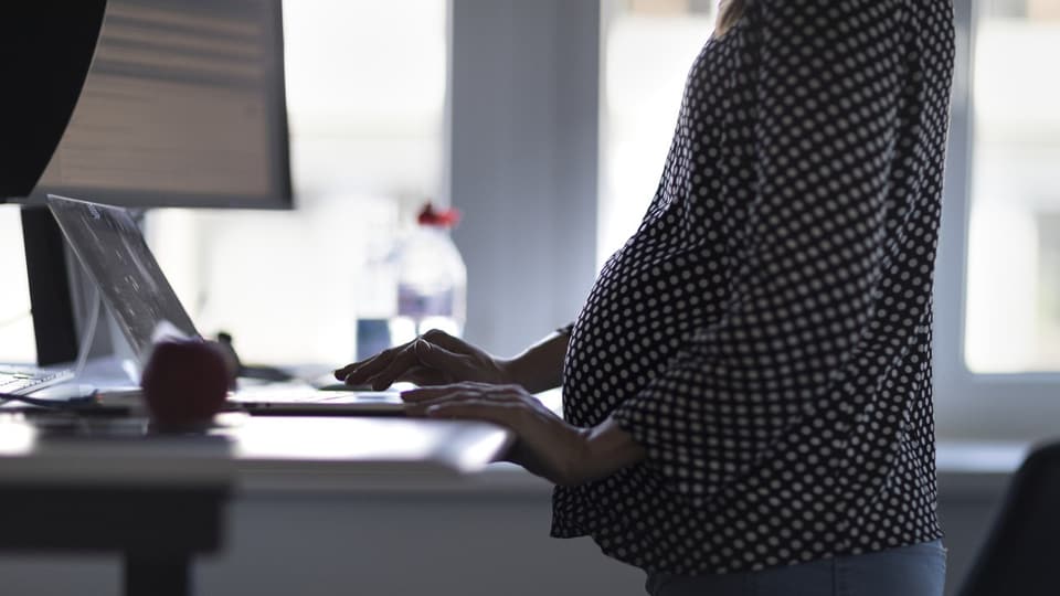 Schwangere Frau arbeitet an einem Stehpult.