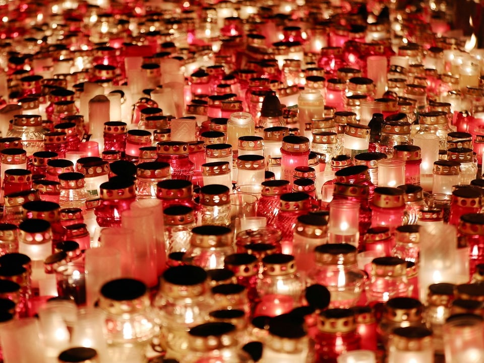 Viele brennende Grabkerzen in Rot und Weiss.