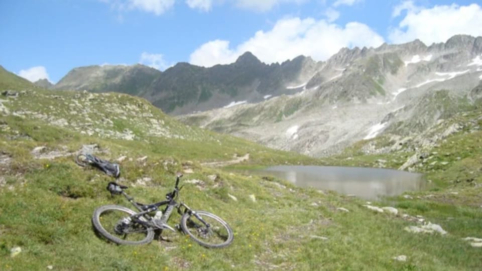 Zwei Mountainbikes liegen neben einem Bergsee im Gras.