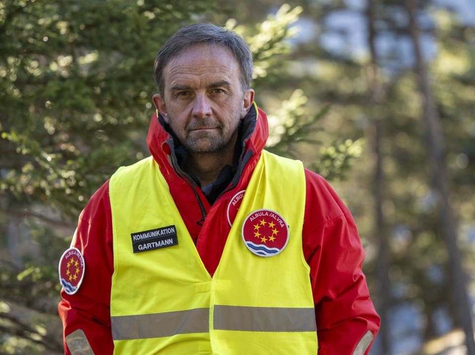 Mann in roter Jacke und gelber Weste im Wald.