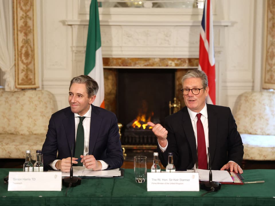 Keir Starmer und Simon Harris sitzen an einem Tisch vor irischer und britischer Flagge.