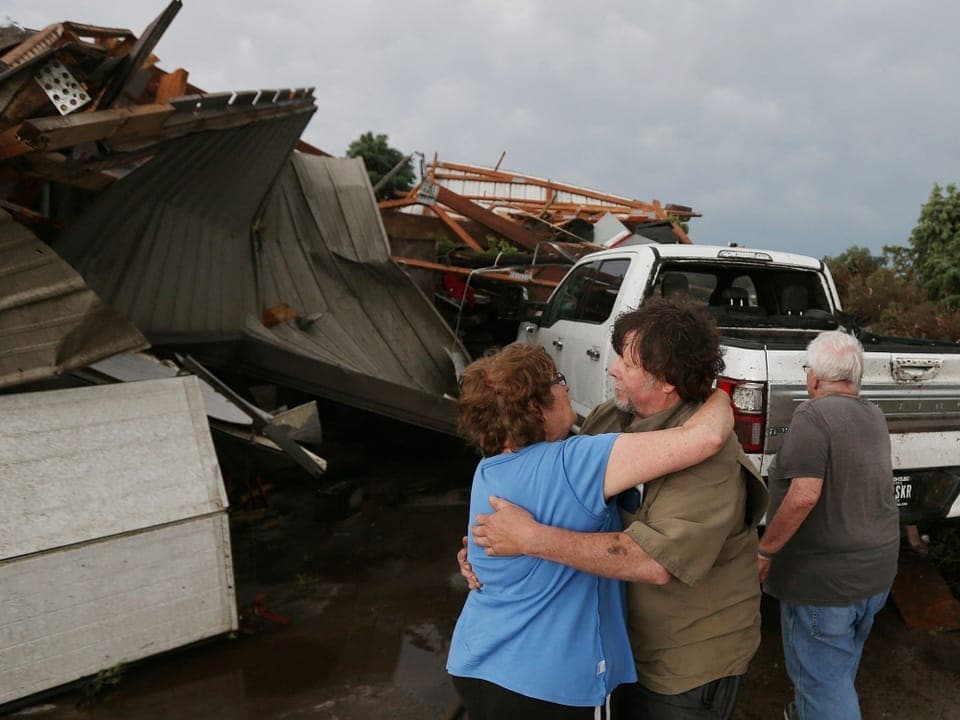 Menschen umarmen sich vor Trümmern nach einem Sturm.