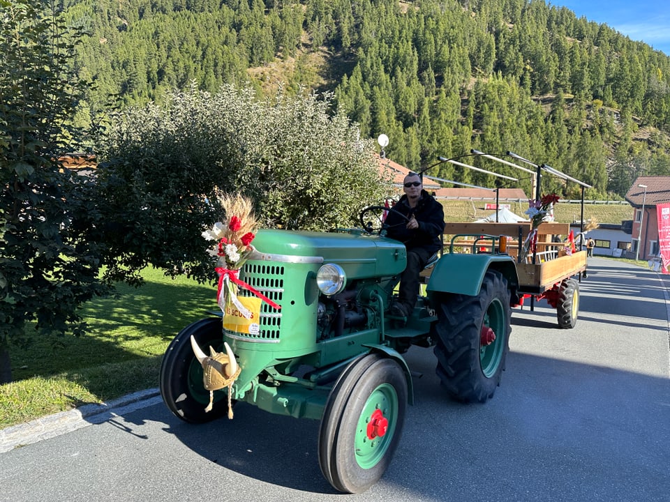 Grüner Traktor mit Anhänger auf Landstrasse, geschmückt mit Blumen und Heu.