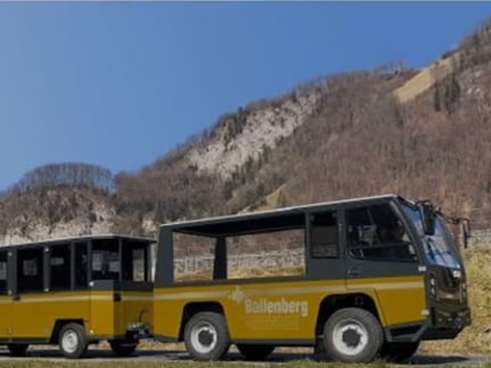 Gelber Bus mit Ballenberg-Beschriftung auf einer ländlichen Strasse vor einem Hügel.