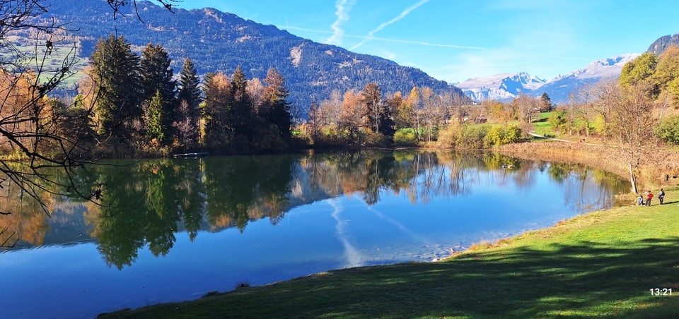 See mit umliegenden Bergen und Bäumen im Herbst.