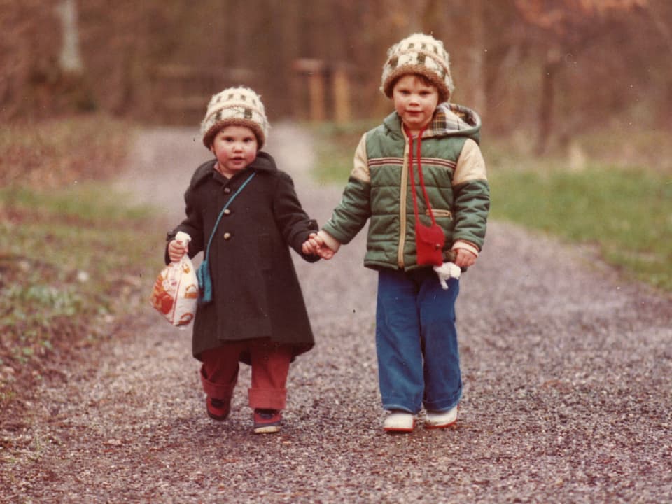 Zwei kleine Mädchen in warmen Jacken und Mützen auf einem Waldweg.