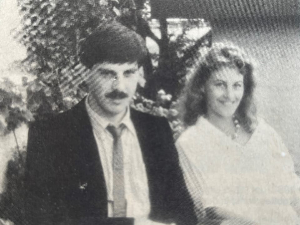 Schwarzweissfoto von einem Mann im Anzug und einer Frau in einem weissen Kleid, die nebeneinander sitzen.