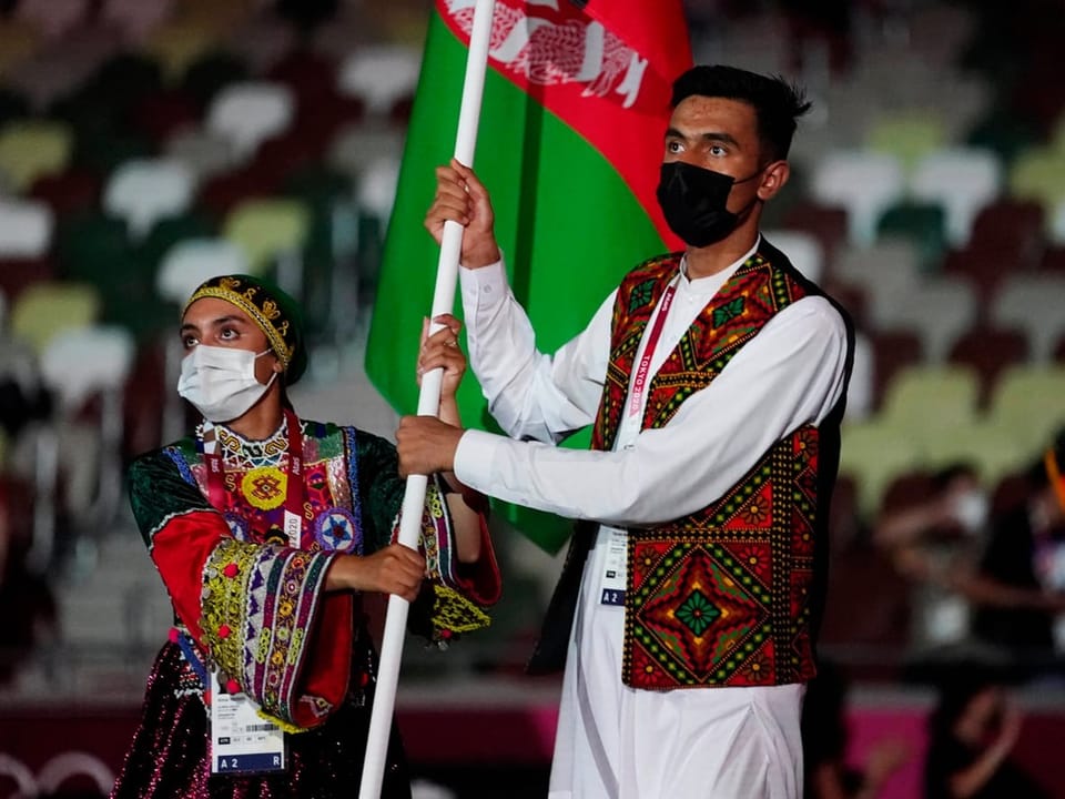 Menschen in traditioneller Kleidung halten eine afghanische Flagge bei einer Zeremonie hoch.