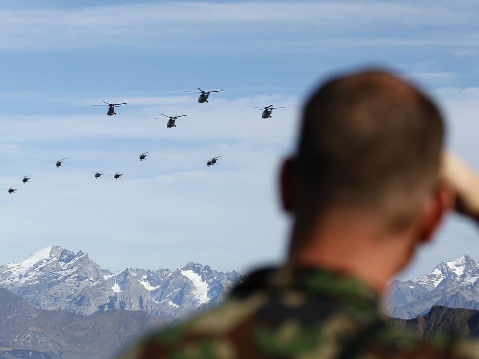 Soldat beobachtet Hubschrauber vor Bergkulisse.