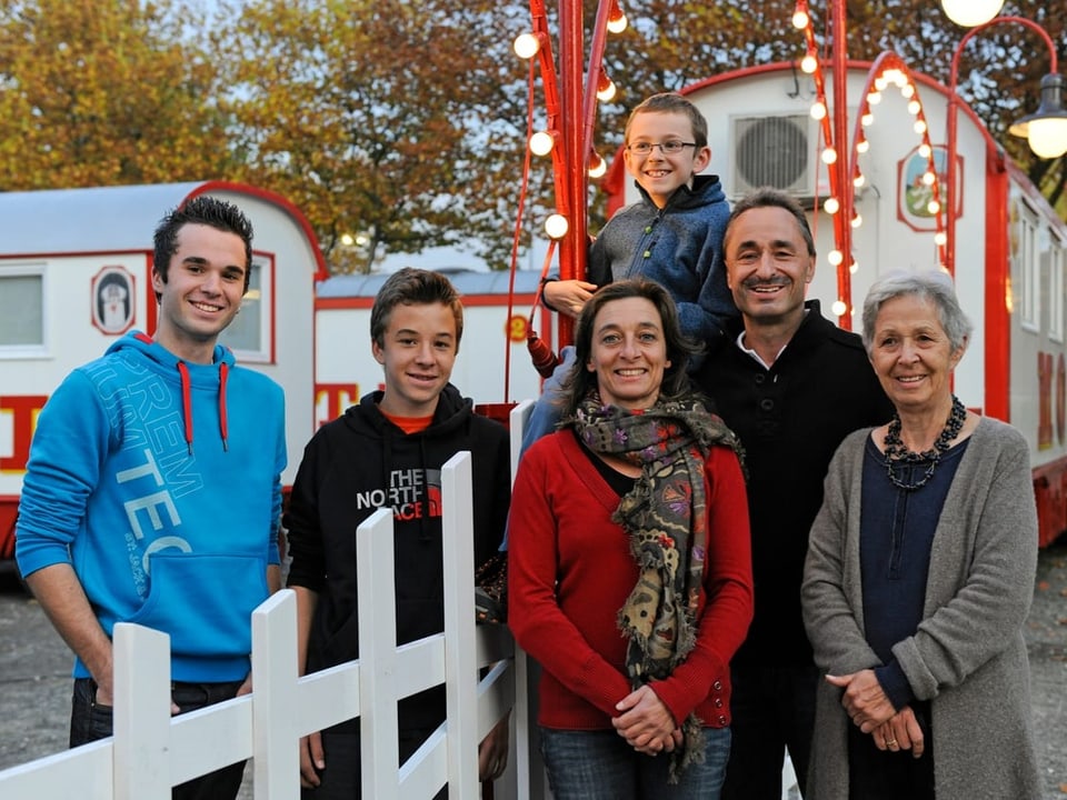 Eine Familie sthet vor einem Zirkuswagen. 