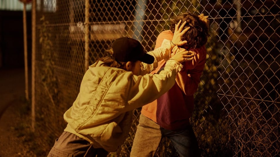 Ein Junge drückt einen anderen an einen Gitterzaun.