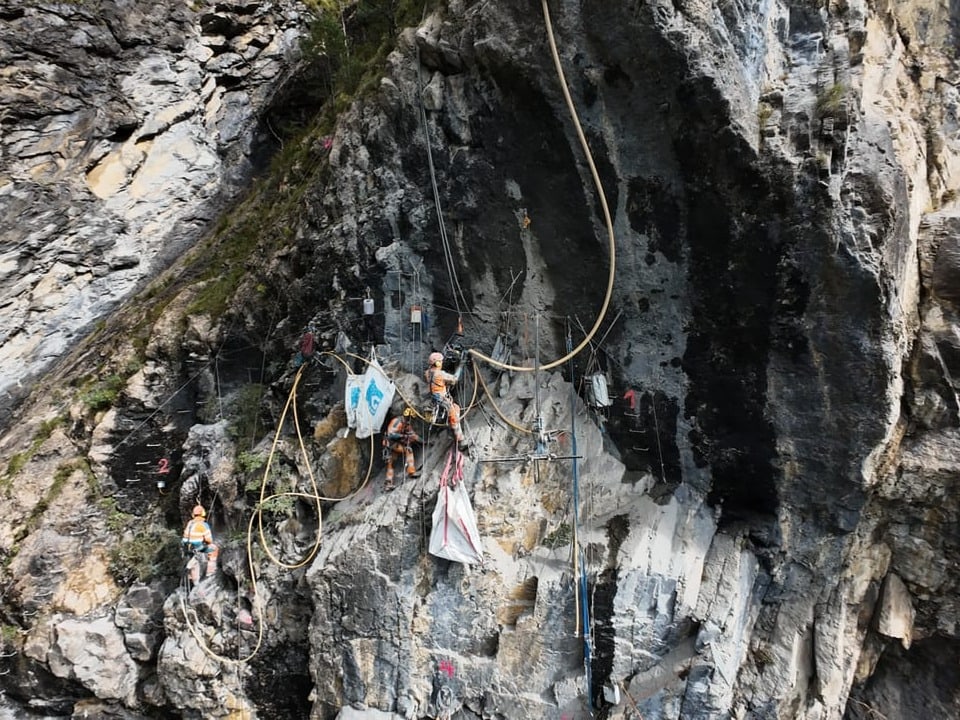 Bauarbeiter klettern an steiler Felswand mit Ausrüstung.