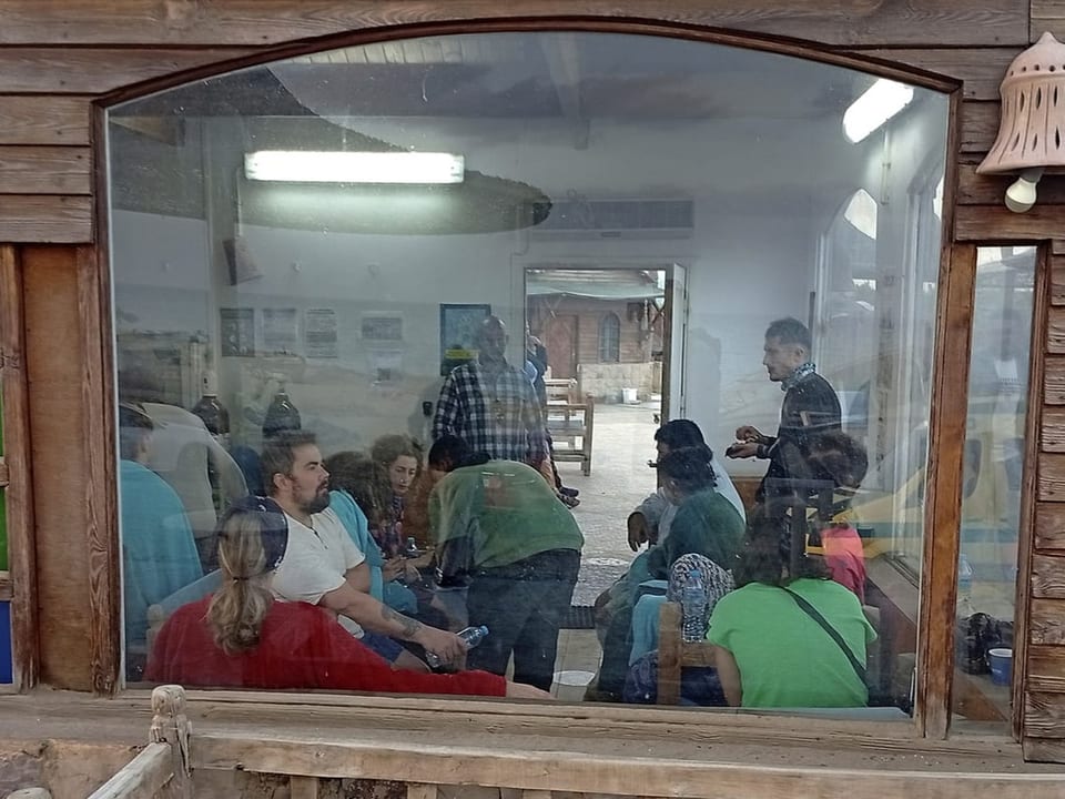 Menschen sitzen und stehen in einem Raum hinter einem grossen Fenster.