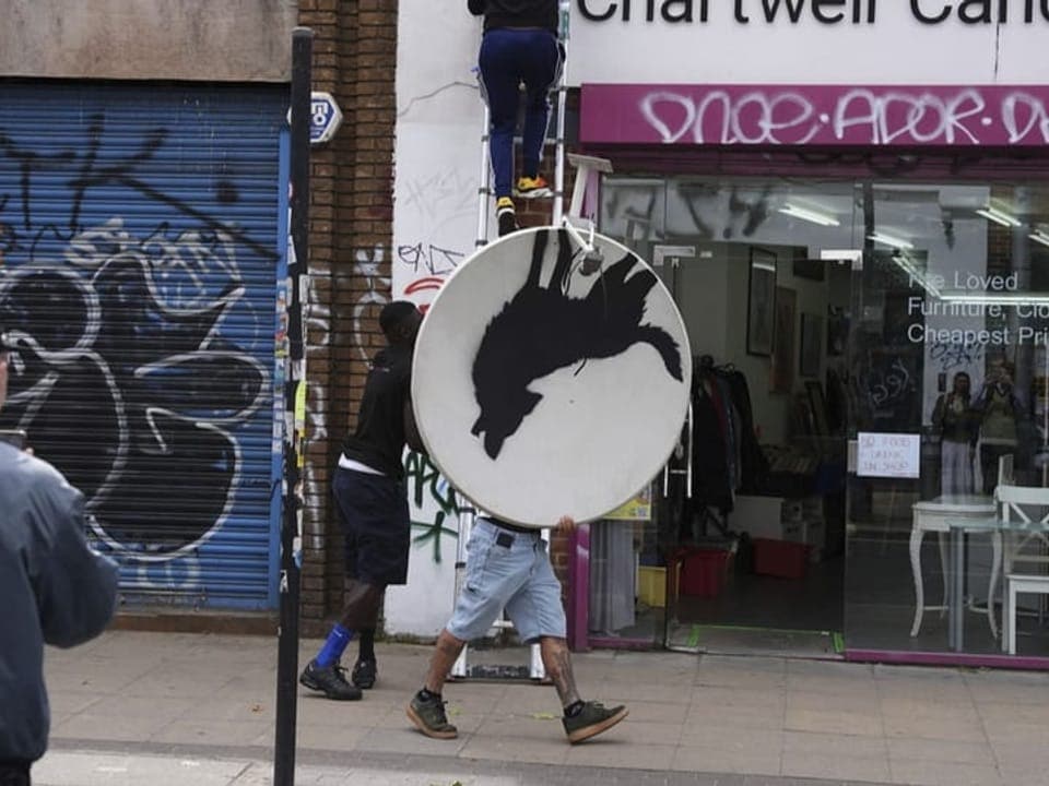 Zwei Männer tragen ein rundes Schild mit Tier-Silhouette.