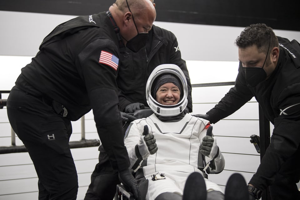 Eine Astronautin in weissem Weltraum-Anzug lächelt glücklich in die Kamera. 