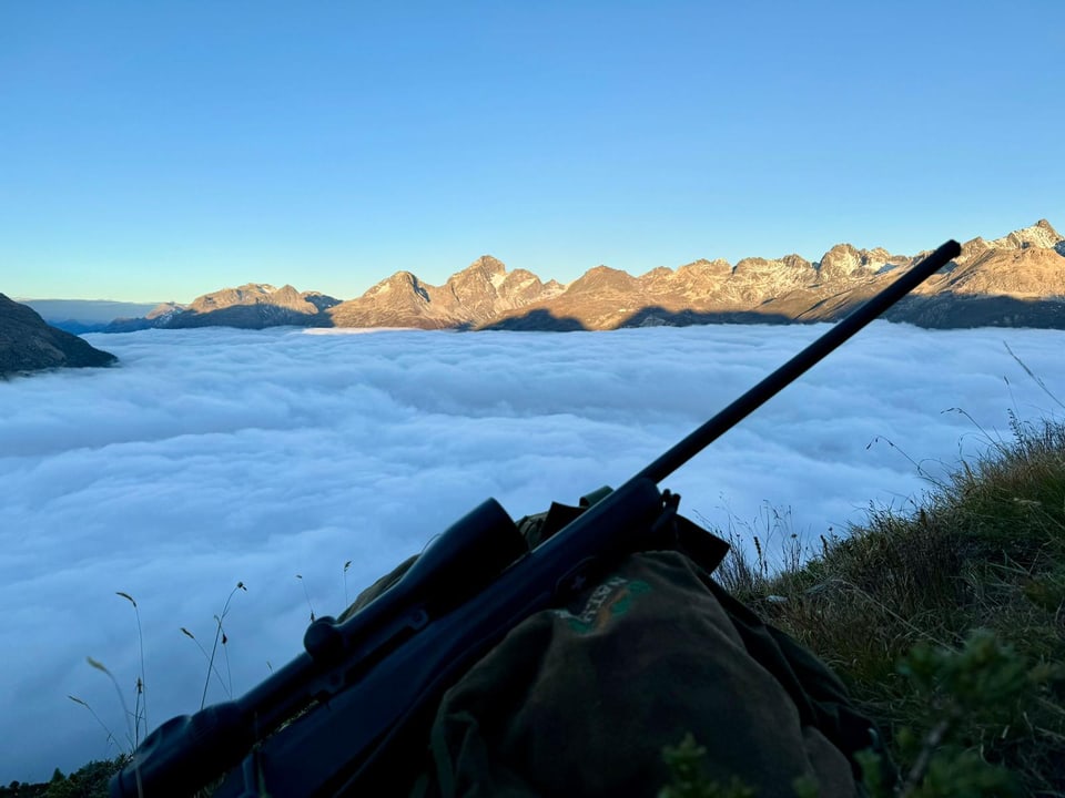 Gewehr auf einer Wiese vor wolkenverhangenen Bergen.