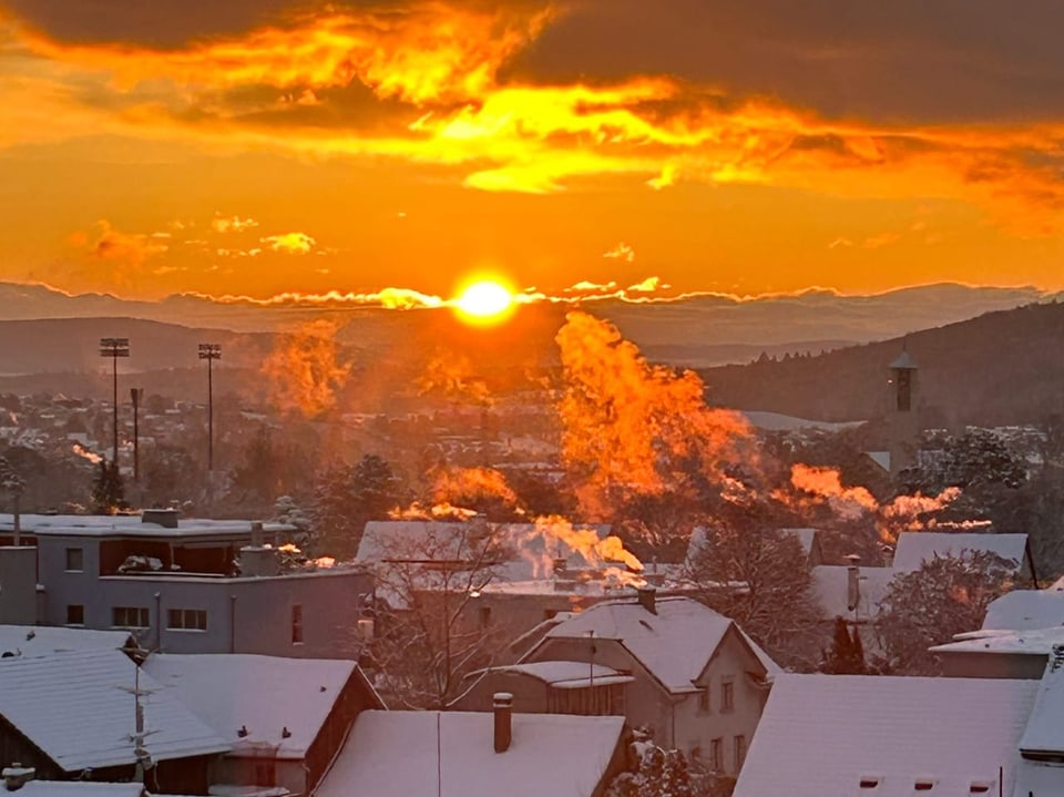 Verschneite Stadtansicht bei Sonnenuntergang mit Rauchschwaden am Himmel.