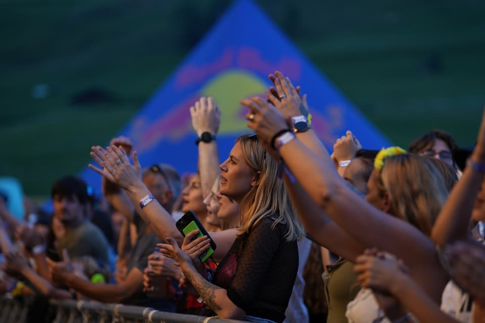 Menschenmenge bei Konzert, erhobene Hände, Beleuchtung aus Bühne.