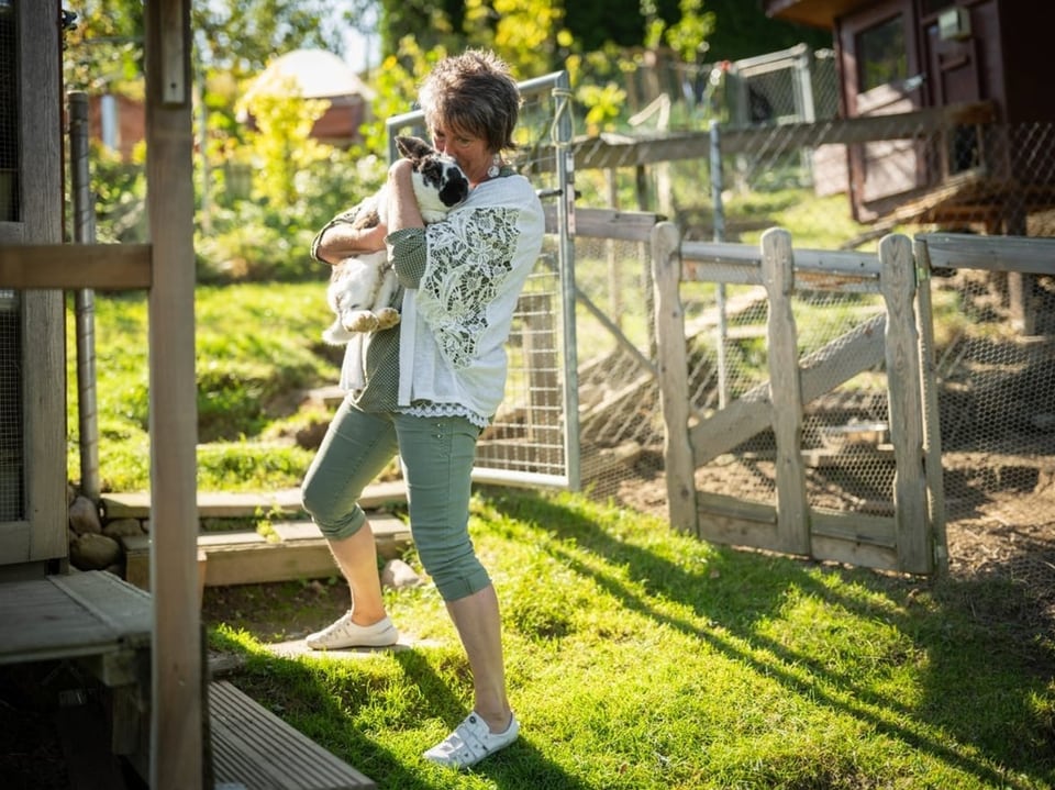 Frau hält Hund im Garten.