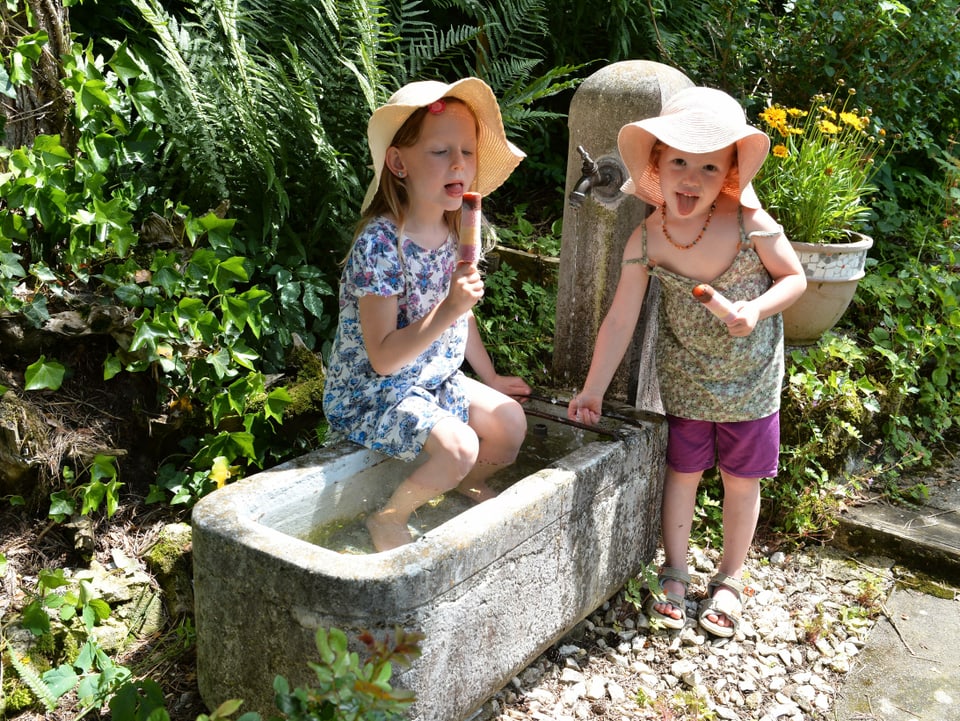 Zwei kleine Mädchen an einem Brunnen mit einem Eis in der Hand.