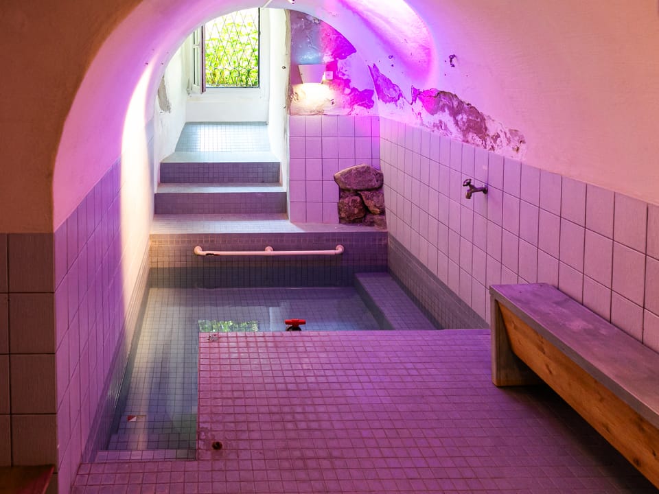 Ein gefülltes Bad mit einem Bänkli und violettem Licht.