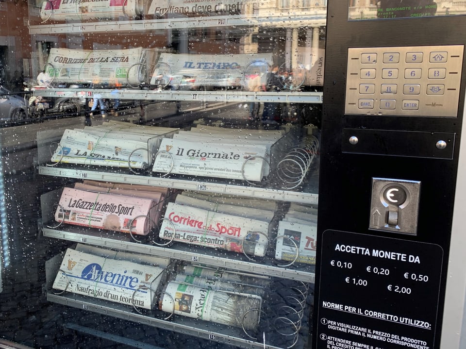 Zeitungsautomat mit italienischen Zeitungen und Münzeinwurf.