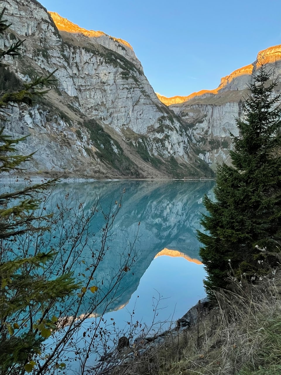 Bergsee mit Spiegelung und Felsen im Hintergrund.