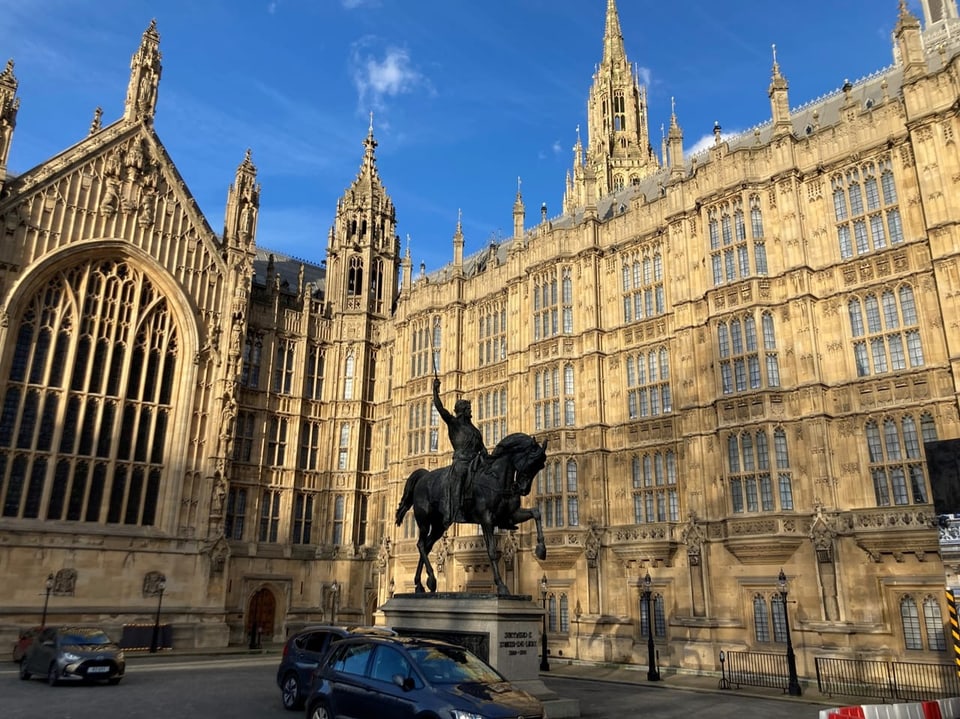 Statue under blue sky in front of Gothic mansion in London.