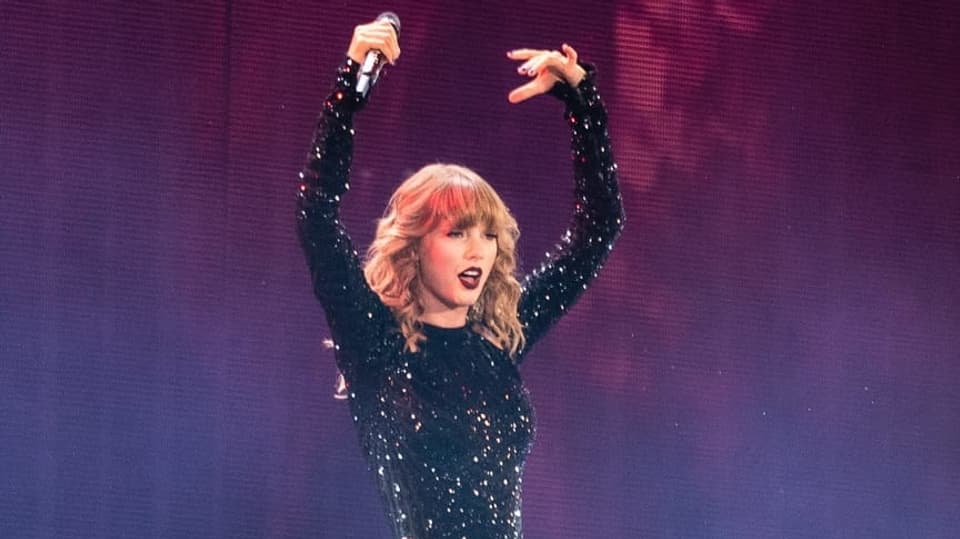 Taylor Swift hält die Hände hoch.