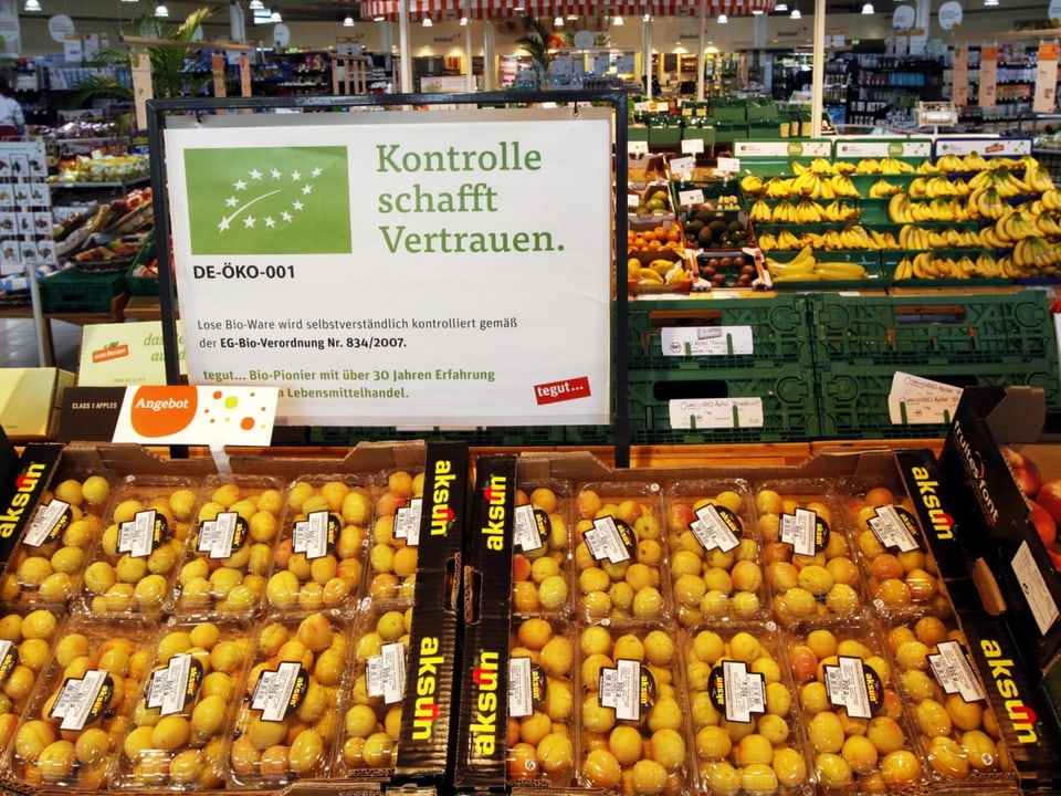 Supermarkt mit Bio-Obst und Infotafel über Kontrolle.