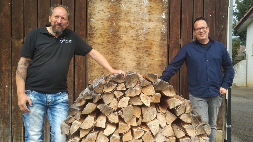 Zwei Männer stehen neben Brennholz