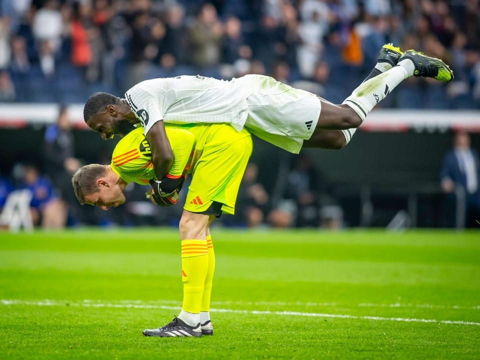 Fussballspieler hebt Torwart auf dem Spielfeld hoch.