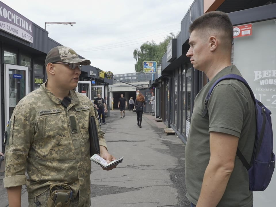 Zwei Männer unterhalten sich in einem Einkaufsviertel, einer in Militäruniform.