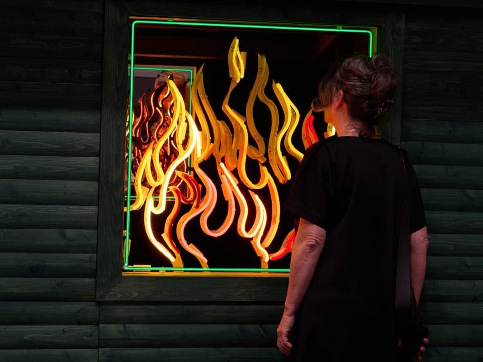 Frau schaut durch Fenster mit buntem Neonflammen.
