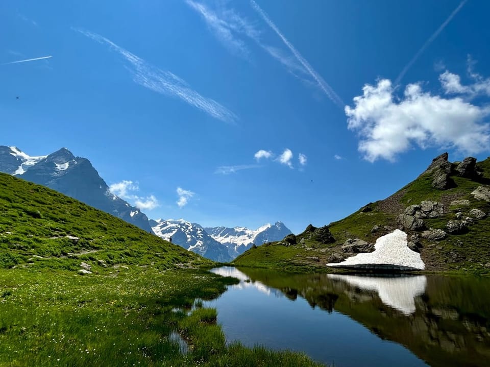 Alpenlandschaft mit kleinem See und Schneeresten.